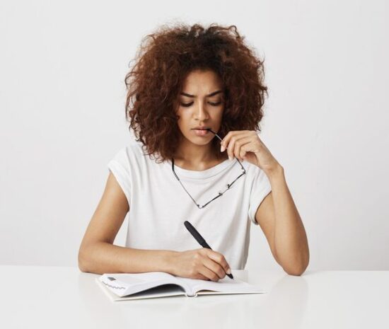 african-girl-thinking-writing-notebook-sitting-table-white-wall-copy-space_176420-11150